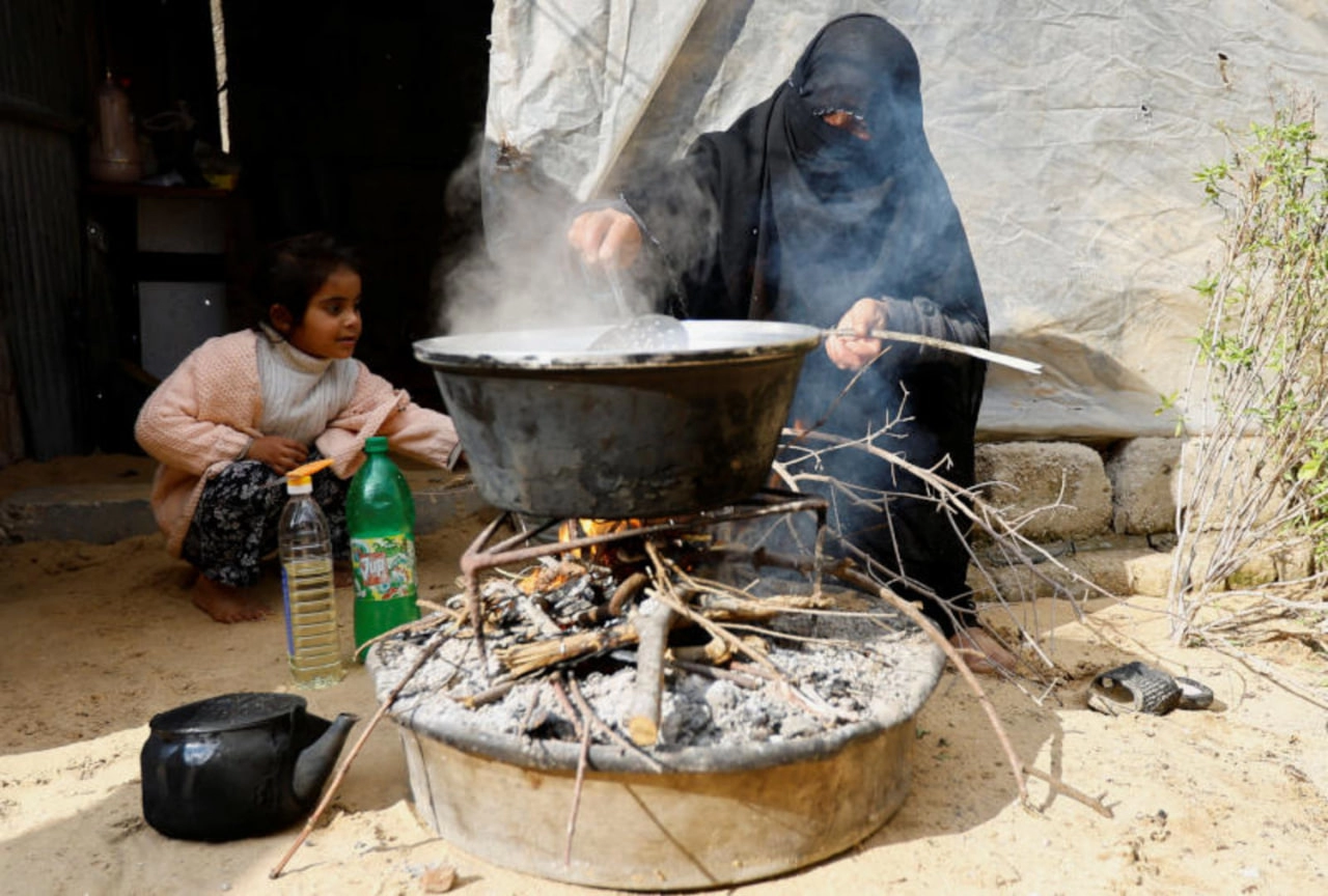 امرأة من غزة تشعل النار وتعد الطعام على الحطب.jpg